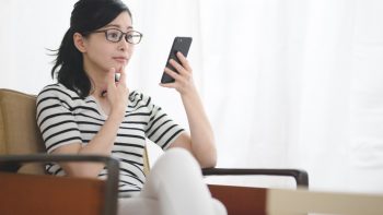 自宅のソファーに座りスマートフォンで仕事を探している様子の女性