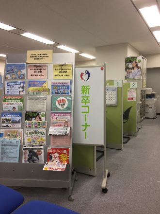 手間にチラシのラックがあり、奥に利用可能な2台のパソコンと1台のプリンターがある、新卒コーナーエリアの画像。